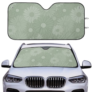 May include: A green car sunshade with a floral pattern of white daisies. The sunshade is shown in a car windshield.