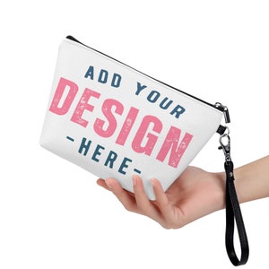 Op de afbeelding: Een witte ritszak met een zwarte rits en een zwarte band. De tas heeft de tekst "ADD YOUR DESIGN -HERE- " erop gedrukt in roze en blauw.