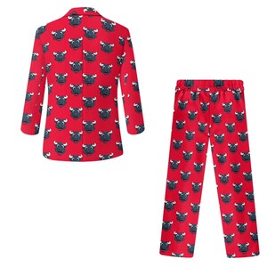May include: Red blazer and matching pants set. The clothing features a repeating pattern of a black bull's head with white horns and accents. The blazer has long sleeves and a button closure. The pants have a drawstring waist.
