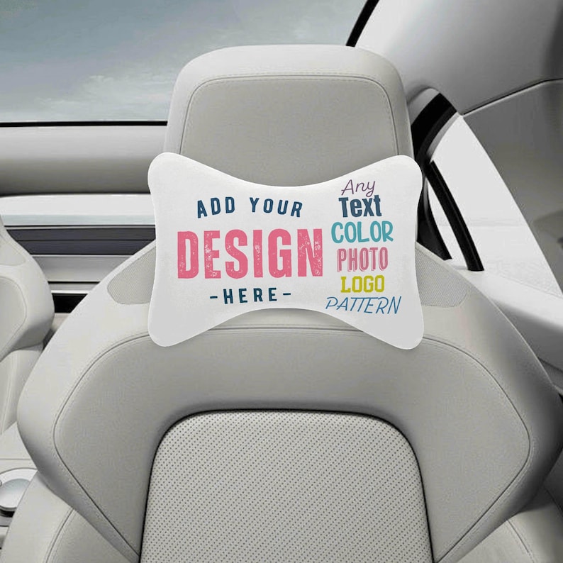 Puede incluir: Coj&iacute;n blanco para reposacabezas de coche con el texto "ADD YOUR DESIGN - HERE-". El texto "DESIGN" es rosa y el resto del texto es azul. El coj&iacute;n est&aacute; en un asiento de coche.