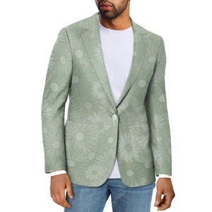 Puede incluir: Una blazer verde claro con un estampado floral de margaritas. La blazer tiene un cierre de un solo botón, solapas con muescas y dos bolsillos delanteros. El diseño floral es de un tono verde más claro, creando un contraste sutil. La blazer se lleva sobre una camiseta blanca y vaqueros azules.