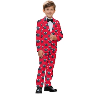 May include: A red suit with a black bull pattern, worn with a white shirt and black bow tie. The suit includes a matching blazer and pants. The boy is wearing black dress shoes. The suit is suitable for a special occasion.