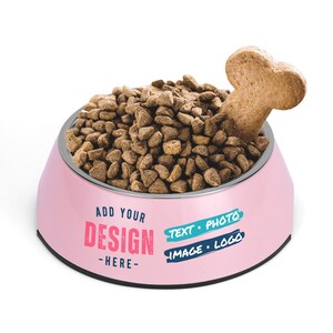 Puede incluir: Tazón rosa para perro con una golosina en forma de hueso que sobresale de la parte superior. El tazón está lleno de comida para perros marrón y tiene el texto "ADD YOUR DESIGN - HERE - TEXT - PHOTO IMAGE - LOGO" impreso en el lateral.