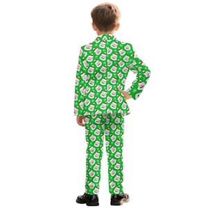 May include: A green Christmas suit with a repeating pattern of Santa Claus faces and snowflakes. The suit includes a blazer and matching pants. The child is wearing black dress shoes.