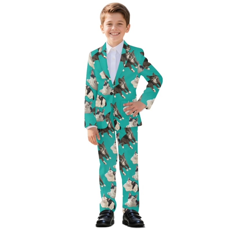 May include: A teal suit featuring a repeating pattern of Boston Terrier dogs. The suit includes a blazer and matching pants. The boy is wearing a white collared shirt and black shoes. The suit is a fun and unique outfit.