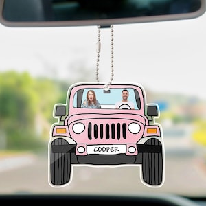 Puede incluir: Un ambientador de coche rosa con forma de Jeep con una foto de una pareja en su interior. El ambientador cuelga de una cadena plateada y tiene el nombre "COOPER" en la parte delantera.
