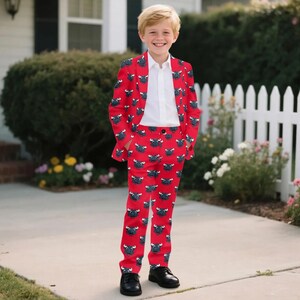 May include: A red suit with a bull pattern, consisting of a blazer and pants, worn with a white collared shirt and black shoes. The suit features a repeating pattern of black bull faces on a red background. The outfit is suitable for a special occasion.