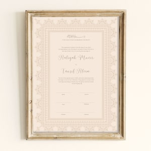 May include: A framed certificate with ornate beige borders and text. The document features elegant calligraphy with names and dates, set against a cream-colored background. The frame is a light gold color.