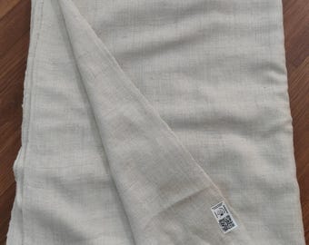 May include: A folded, off-white woven blanket with a fringed edge. The blanket is made of a textured fabric and has a tag in the corner. The blanket is displayed on a wooden surface.