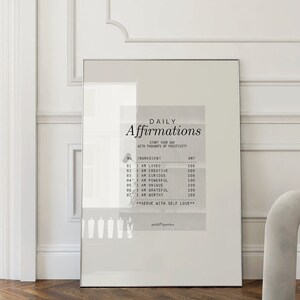 K&ouml;nnte beinhalten: Ein gerahmter Druck mit wei&szlig;em Hintergrund und schwarzem Text, der "T&auml;gliche Affirmationen" lautet und eine Reihe von Affirmationen auflistet. Der Druck h&auml;ngt an einer wei&szlig;en Wand in einem Raum mit einem grauen Stuhl.