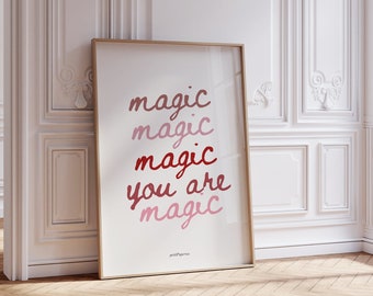 May include: A rectangular framed wall art print with a light wood frame. The white background features the text "magic" repeated three times in varying shades of pink and red, followed by the text "you are magic" in red and pink script.