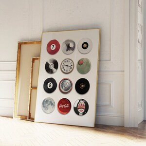 May include: A framed print with a white background and 12 circular images. The images include a red billiard ball with the number 7, a clock face, a can of soda, a Coca-Cola logo, a Chanel logo, and a woman's face.
