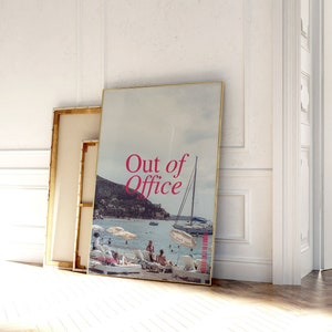 May include: A framed print with a photo of a beach scene with a sailboat and people on the beach. The text "Out of Office" is printed in pink on the photo.