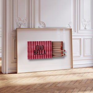 May include: A framed print of a red and white striped matchbox with the text "Ciao Bella" printed on the front. The matchbox is open and contains a row of matches.