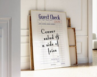 Puede incluir: Un cartel blanco enmarcado con texto negro que dice "Guest Check" y "Ceasar salad & a side of fries". El cartel está colgado en una pared blanca en una habitación con suelo de madera.