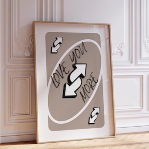 May include: A brown and white Uno card with the text "Love You More" and a reversed arrow symbol. The card is framed in a gold frame.