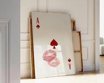 May include: A framed art print featuring the Ace of Spades playing card design. The artwork includes a red spade symbol, the letter "A", and a pair of pink lips. The print has a gold frame and is leaning against a wall.
