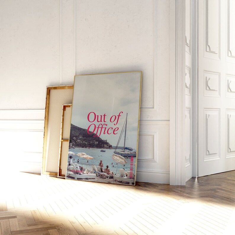 May include: A framed print with a photo of a beach scene with a sailboat and people on the beach. The text "Out of Office" is printed in pink on the photo.