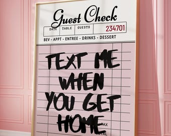 May include: A framed print with a pink background and the words "TEXT ME WHEN YOU GET HOME" in bold black letters. The top of the print reads "Guest Check" with a number. The print is displayed on a pink wall.