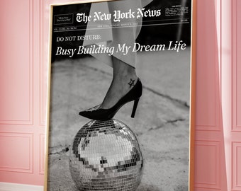 Könnte beinhalten: Ein Schwarzweißfoto eines Frauenfußes, der einen hochhackigen Schuh trägt und auf einer Discokugel steht. Das Foto ist gerahmt und hat den Text "The New York News" und "Do Not Disturb: Busy Building My Dream Life" darauf gedruckt.