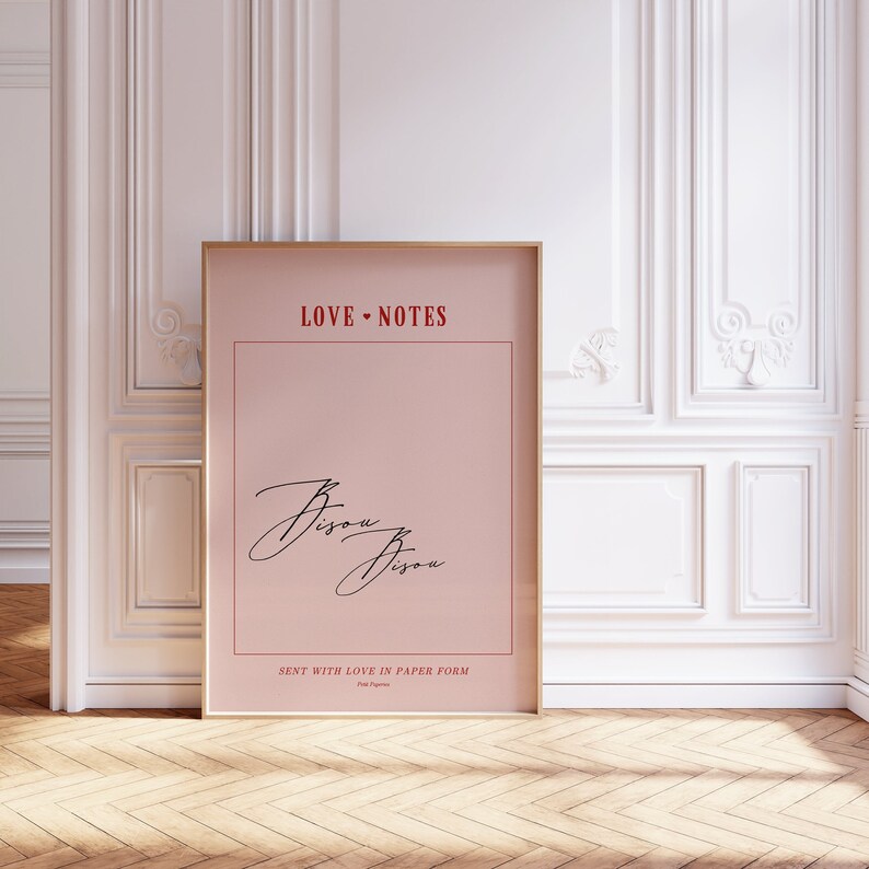 May include: A pink poster with a gold frame. The poster has the text "LOVE NOTES" in red at the top and the word "Bisou" written twice in black cursive. The bottom of the poster says "SENT WITH LOVE IN PAPER FORM" in red.
