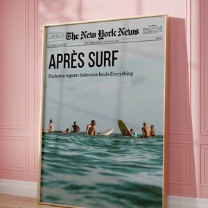 May include: A framed print featuring a vintage-style newspaper headline, "APR&Egrave;S SURF," with a photo of surfers in the ocean. The text "Exclusive report: Saltwater heals Everything" is also visible. The print is in a gold frame.