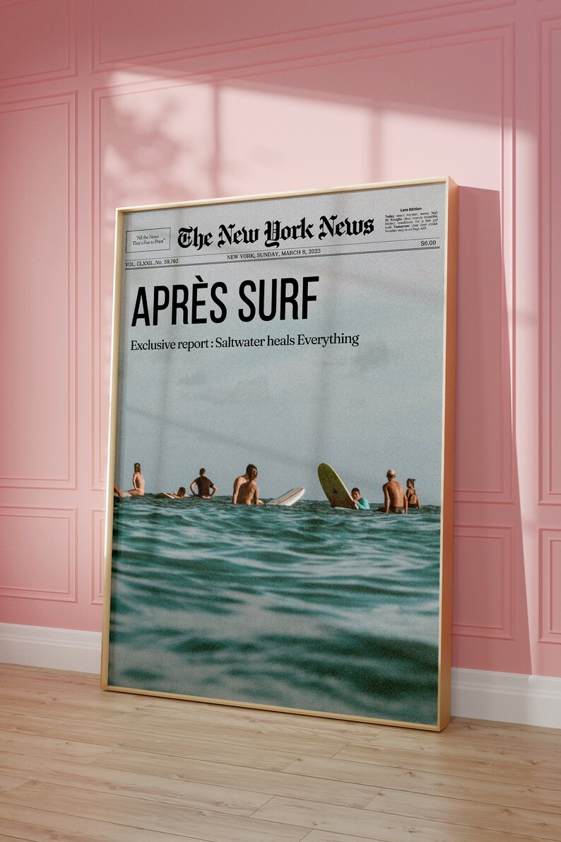 May include: A framed print featuring a vintage-style newspaper headline, "APR&Egrave;S SURF," with a photo of surfers in the ocean. The text "Exclusive report: Saltwater heals Everything" is also visible. The print is in a gold frame.