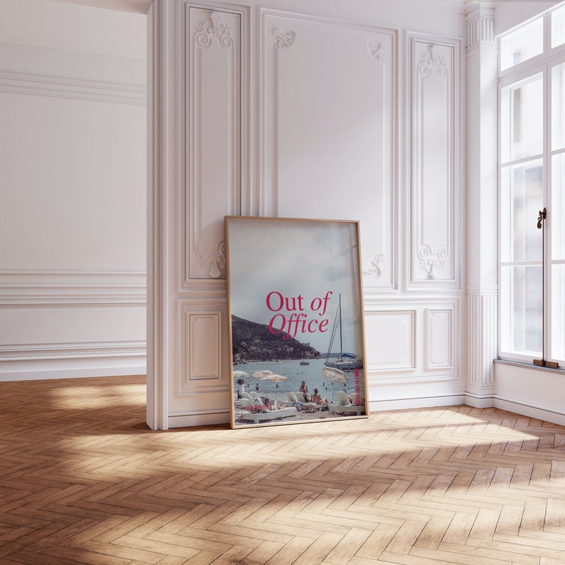 May include: A framed poster with a photograph of a beach scene with people relaxing on the sand and a sailboat in the water. The text "Out of Office" is printed in pink on the poster.