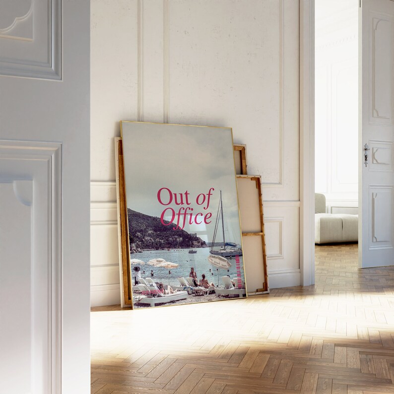 May include: A framed poster with a photograph of a beach scene with a sailboat and people on the beach. The poster has the text "Out of Office" in pink letters.