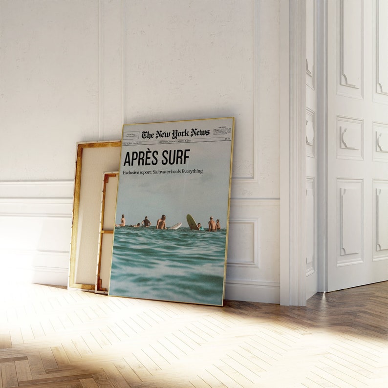 May include: A framed print of a newspaper front page titled "The New York News" with the headline "APR&Egrave;S SURF." The image shows people surfing in the ocean. A blank canvas with a gold frame leans against the wall.
