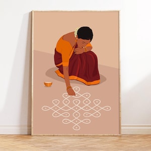 Op de afbeelding: Een ingelijste kunstdruk toont een vrouw in traditionele Indiase kleding, knielend om een wit geometrisch patroon op een lichtbruin oppervlak te creëren. Ze draagt een oranje blouse en een bordeauxrode rok. Een kleine oranje kom staat in de buurt.