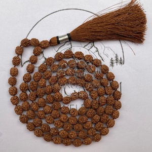 May include: A brown mala necklace with a tassel. The necklace is made of small, round, textured beads. The tassel is a darker shade of brown and is attached to the necklace with a silver-colored metal piece.