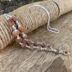 May include: A silver necklace with multiple strands of brown, textured beads. The beads are strung together with silver wire and connected to a delicate silver chain. The necklace is displayed on a roll of twine.