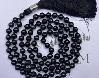 May include: A black beaded mala necklace with a large black tassel. The beads are round and appear to be made of a polished stone. The tassel is attached to the necklace with a silver-colored metal piece.