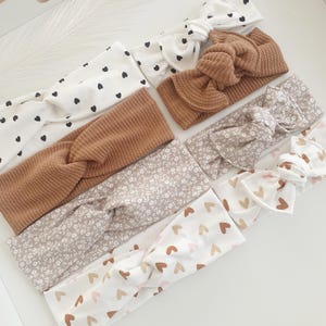 Puede incluir: Un conjunto de ocho diademas con diferentes patrones. Las diademas están hechas de una tela suave y elástica y presentan una variedad de colores y diseños, incluyendo lunares negros y blancos, tejido marrón, estampado floral y corazones rosas y marrones.