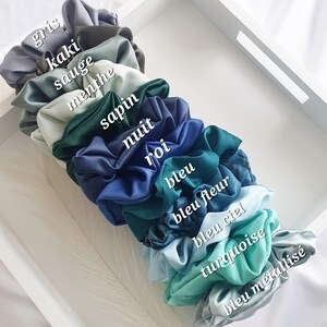 Puede incluir: Una pila de 12 scrunchies de sat&eacute;n de colores en tonos de azul, verde y gris. Los scrunchies est&aacute;n etiquetados con palabras francesas que describen sus colores, incluyendo "gris", "kaki", "sauge", "menthe", "sapin", "nuit", "roi", "bleu", "bleu fleur", "bleu ciel", "turquesa" y "bleu metalizado".