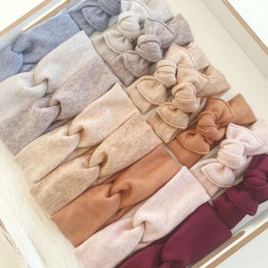 Może przedstawiać: Kolekcja dziesięciu spiętych opasek do włosów w różnych kolorach, w tym beżowym, brązowym, bordowym i szarym. Opaski wykonane są z miękkiej, elastycznej tkaniny i idealnie nadają się do dodania odrobiny stylu do każdego stroju.