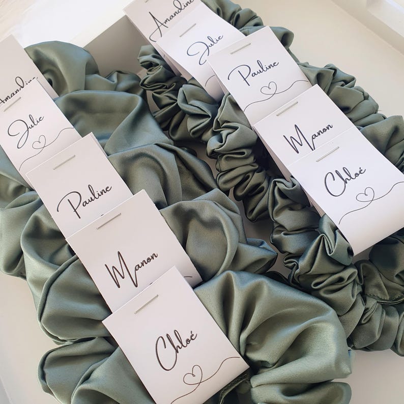 Puede incluir: Conjunto de scrunchies de sat&eacute;n verde con etiquetas de nombre personalizadas. Las etiquetas son blancas con caligraf&iacute;a negra e incluyen los nombres: Amandine, Julie, Pauline, Manon y Chloe.