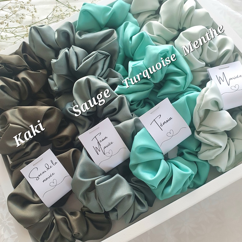 Puede incluir: Surtido de scrunchies de sat&eacute;n en tonos de verde, turquesa y menta. Cada scrunchie tiene una peque&ntilde;a etiqueta blanca con texto en franc&eacute;s, incluyendo "Team Mari&eacute;e", "Soeur de la Mari&eacute;e", "T&eacute;moin" y "Mari&eacute;e".
