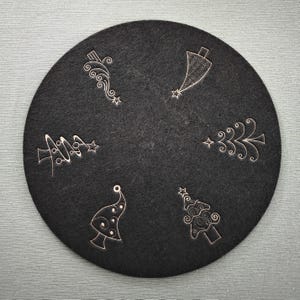 May include: A black felt coaster with five white, stylised Christmas tree designs.