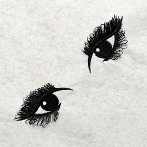 Könnte beinhalten: Zwei schwarze gestickte Augen mit Wimpern auf weißem Hintergrund.