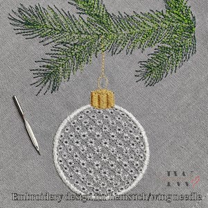 Könnte beinhalten: Gesticktes Weihnachtsbaumschmuck-Design mit goldener Kappe, hängend an einem grünen Kiefernzweig. Der Schmuck ist weiß mit einem detaillierten Muster. Links ist eine silberne Nadel. Text unten: Stickdesign für Hohlsaum-/Flügelnadel.