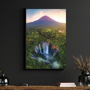 May include: An aerial view of a waterfall cascading down a lush green mountainside. A hot air balloon floats in the sky above the mountain, which is bathed in the warm glow of the setting sun.