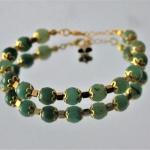 May include: A double-strand bracelet with green gemstone beads and gold accents. The beads are oval-shaped and have a smooth, polished finish.