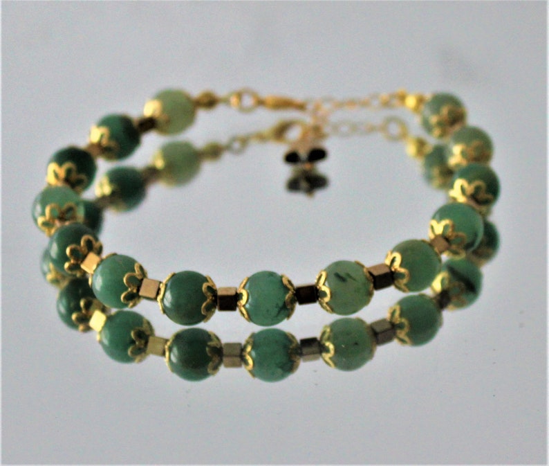 May include: A double-strand bracelet with green gemstone beads and gold accents. The beads are oval-shaped and have a smooth, polished finish.