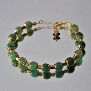 May include: A double-strand bracelet with green oval beads and gold accents. The bracelet has a gold clasp and a small gold charm.