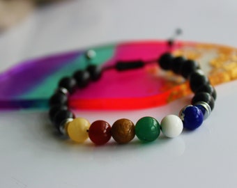 May include: A bracelet with black lava beads and seven colorful gemstone beads. The beads are yellow, red, brown, green, white, and blue.
