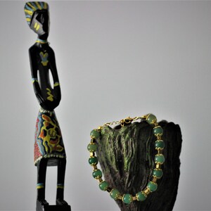 May include: A green gemstone bracelet with gold accents on a wooden stand. The bracelet is made of round beads and has a clasp closure.
