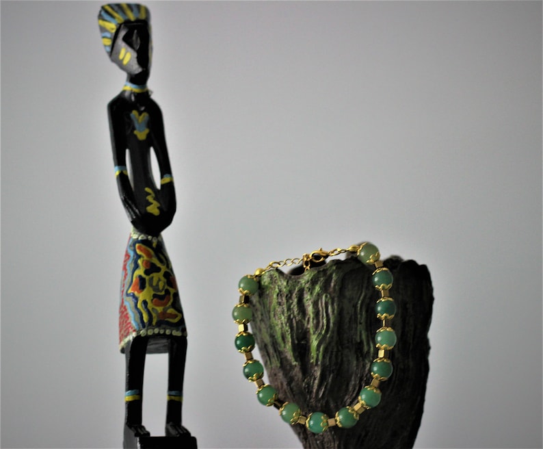 May include: A green gemstone bracelet with gold accents on a wooden stand. The bracelet is made of round beads and has a clasp closure.