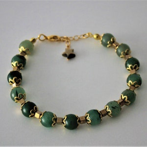May include: A green gemstone bracelet with gold accents and a star charm. The bracelet is made of round beads with a gold filigree design.